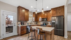 A modern kitchen with wooden cabinets, stainless steel appliances, and a central island with stools.