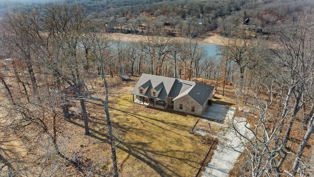A two-story house with a stone exterior and a dark roof, surrounded by trees and a small body of water.