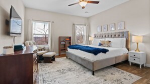 A bedroom with a bed, bedside tables, a desk, a chair, a ceiling fan, and a window with blinds.