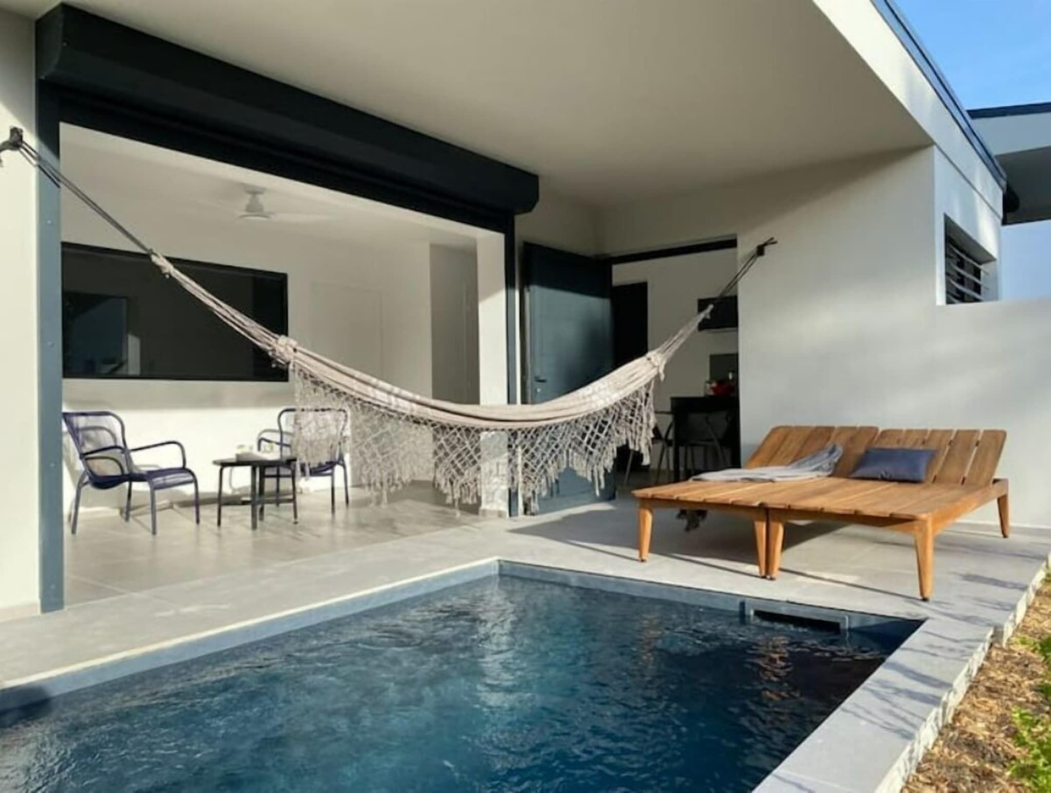 A modern outdoor pool area with a hammock, lounge chairs, and a dining area.