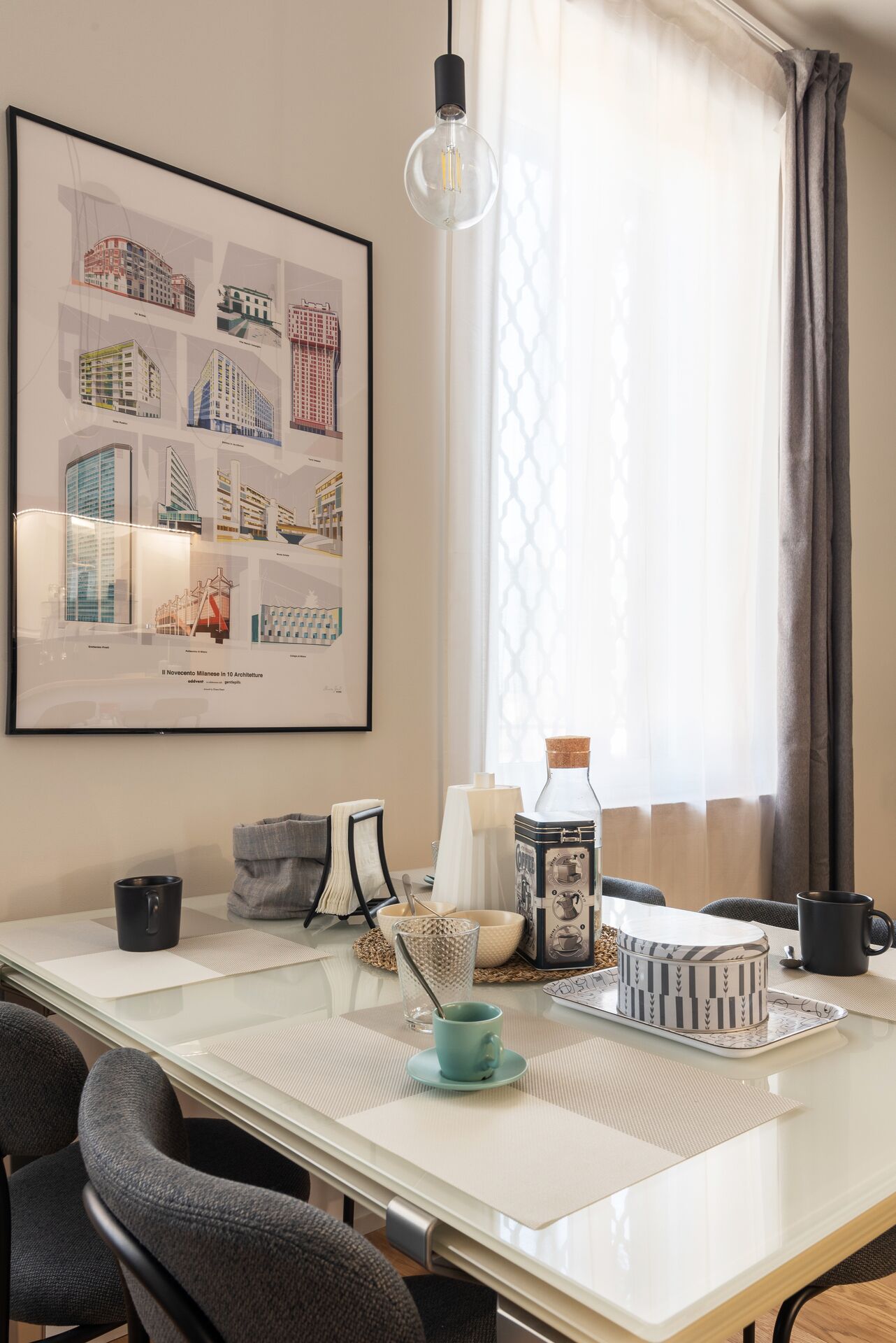Un comedor moderno con una mesa de vidrio, láminas arquitectónicas enmarcadas y una lámpara colgante.