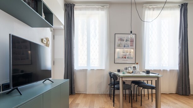 Ein modernes Wohnzimmer mit Flachbildfernseher, einem Esstisch mit Stühlen und einem gerahmten Stadtbild an der Wand.
