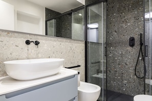 Une salle de bain moderne avec un grand lavabo blanc, des toilettes et une douche séparée par une paroi de verre.