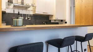 Eine moderne Küche mit Holzarbeitsplatte, hängenden Küchenutensilien und einer Bar mit zwei Stühlen.