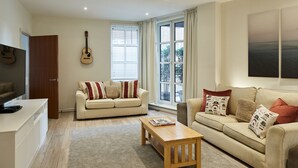 A living room with two sofas, a coffee table, a TV, and a guitar on the wall. - Castle Retreat City Centre Near Train & Parking (Winchester)