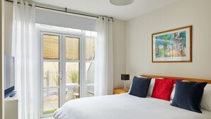 A hotel room with a large bed, a television on a stand, a bedside table with a lamp, and a sliding glass door leading to an outdoor area. - Castle Retreat City Centre Near Train & Parking (Winchester)