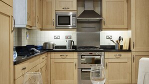 A modern kitchen with wooden cabinets, stainless steel appliances, and a dining area with a table set for two. - Castle Retreat City Centre Near Train & Parking (Winchester)