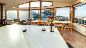 Een ruime eethoek met een grote tafel, meerdere stoelen en uitzicht op zee.