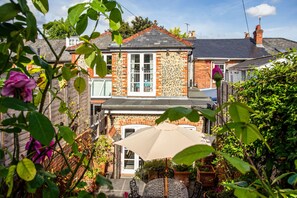 A two-story house with a brick facade, a tiled roof, and a front garden with potted plants and a patio table with an umbrella. - Peaceful Elevated Residential Area - Walk to City (Winchester)