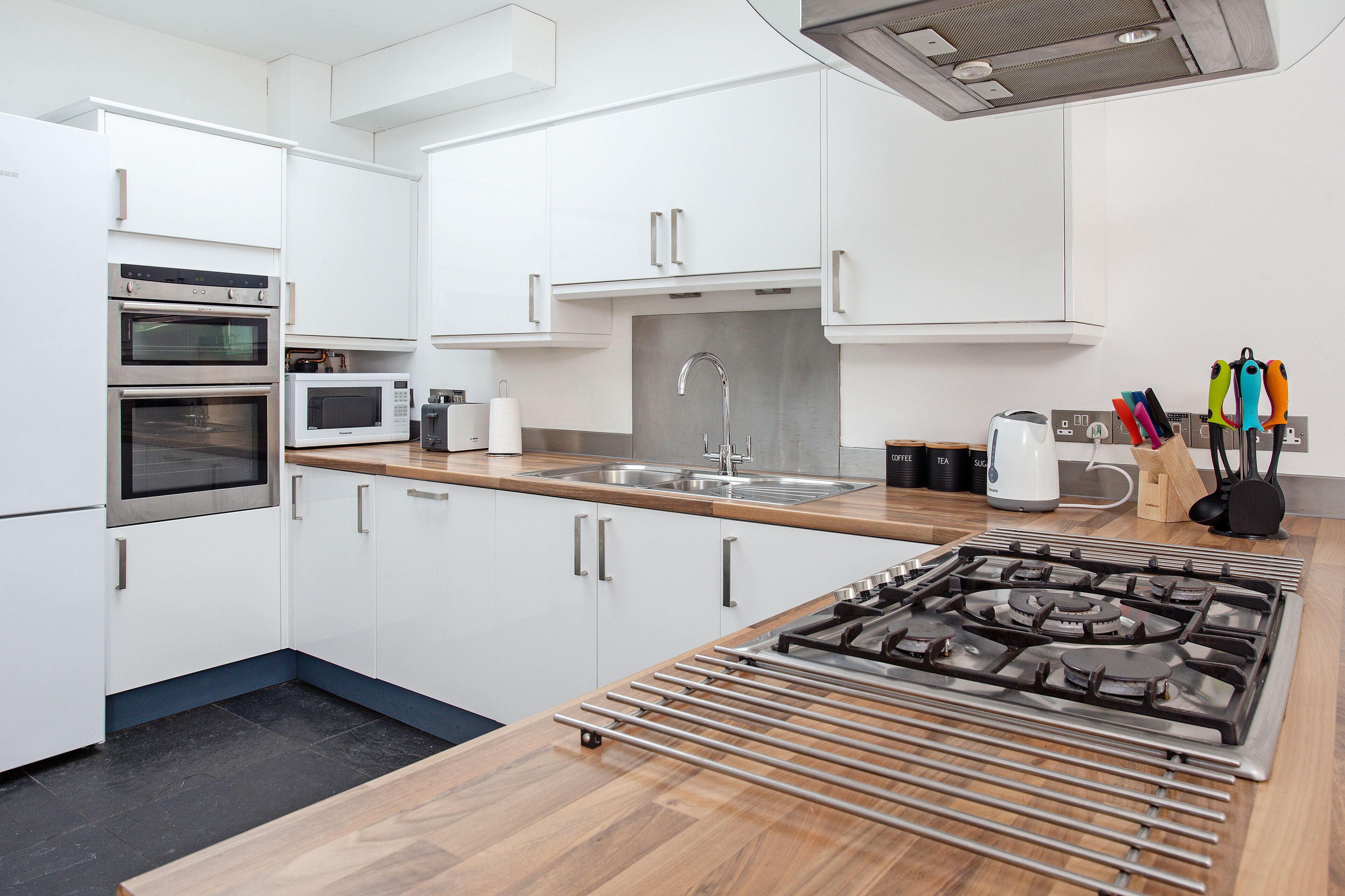 A modern kitchen with white cabinets, stainless steel appliances, a wooden countertop, and a gas stove.