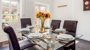 Un coin repas avec une table en verre, des fauteuils en cuir et un vase rempli de tournesols.