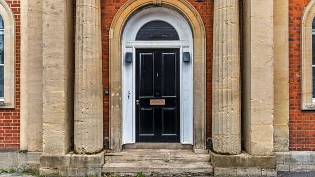 A building entrance with a black door, flanked by two columns, and an arched window above. - Unique Property in the Heart of Winchester (Winchester)