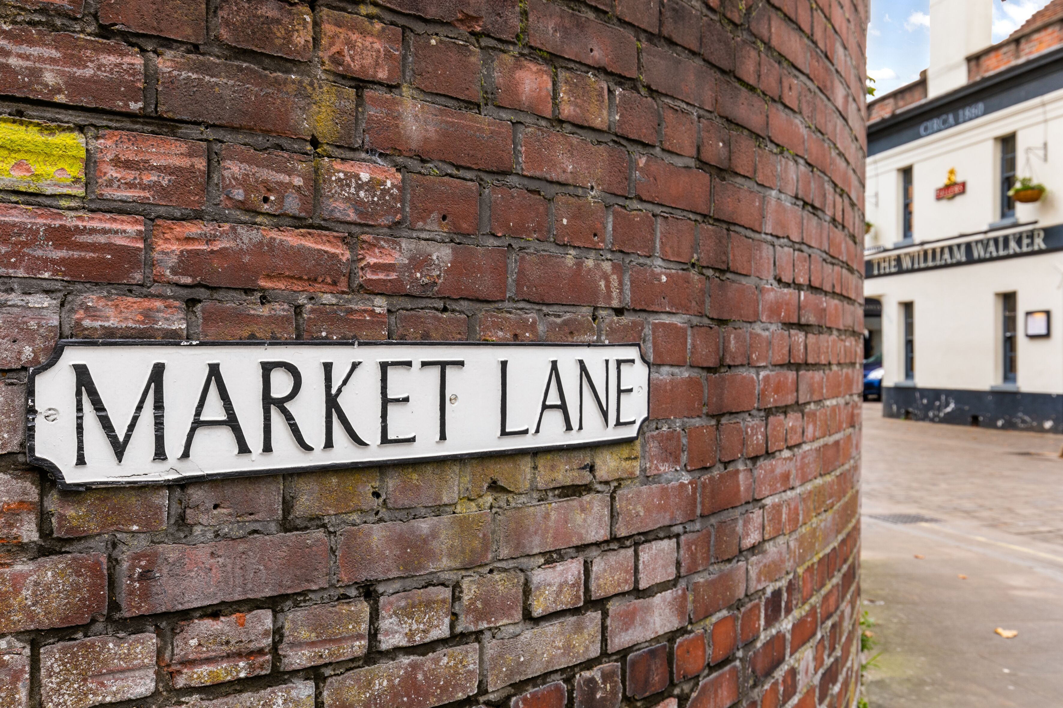 Tiiliseinä, jossa on katukyltti, jossa lukee: ”MARKET LANE”.