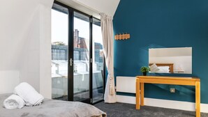 A modern bedroom with a bed, a wooden bedside table, a small bedside plant, a white nightstand, and a large mirror. - Unique Property in the Heart of Winchester (Winchester)