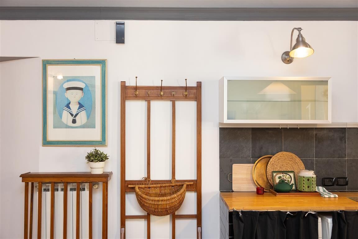 A kitchen with a wooden counter, a hanging basket, a framed picture, and a wall-mounted light fixture.