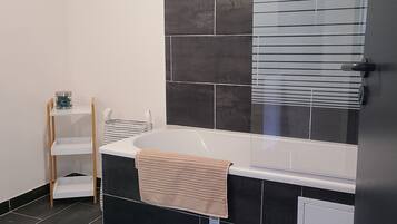 Une salle de bain avec une baignoire, une serviette et une étagère.
