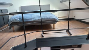 Kompakti, moderni asunto, jossa on parvelle sijoitettu makuuhuone, pieni keittiö ja ruokailutila värikkäillä tuoleilla.