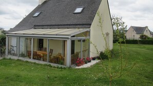 A house with a sloped roof, a glass conservatory, and a garden with potted plants. - DETACHED HOUSE 100 M2 ON A 936 M2 ENCLOSED PLOT AT THE END OF A CUL-DE-SAC (Porspoder)