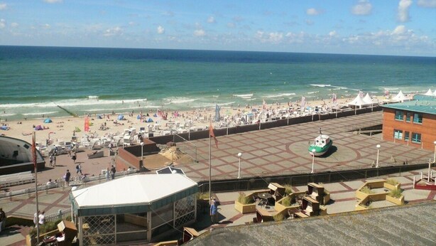 A beachside promenade with a view of the ocean, a covered seating area, and a small boat docked on the promenade. - House Metropol 254, OB (Westerland)