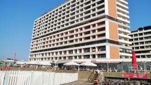 A multi-story hotel with a grid-like facade, balconies on each floor, and a covered outdoor seating area with umbrellas. - House Metropol 254, OB (Westerland)
