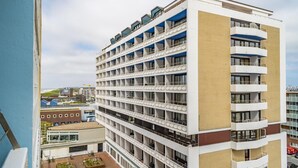 A multi-story hotel with a modern design, featuring balconies on each floor and a courtyard with seating areas.