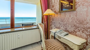 A room with a view of the sea, a white radiator, a desk with a telephone, and a lamp.
