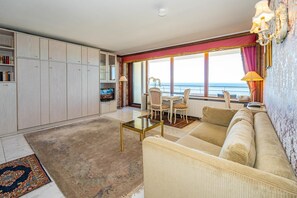 A spacious living room with a sofa, a coffee table, and a dining area with chairs. There is a large window with a view of the sea. - Haus Metropol, App. 097 WB -lage: Das Haus Metropol Steht Direkt am Strand von Westerland Zwischen den Beiden Fußgängerzonen. In Unmittelbarer Nähe Befinden Sich die "sylter Welle" und das "syltness-center". Das Appartement Befindet Sich in der (Westerland)