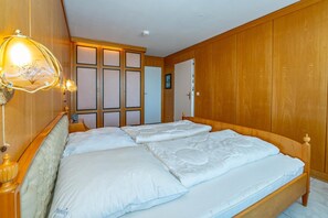 A double bed with white linens in a room with wooden paneling and a wooden door. - Haus Metropol, App. 097 WB -lage: Das Haus Metropol Steht Direkt am Strand von Westerland Zwischen den Beiden Fußgängerzonen. In Unmittelbarer Nähe Befinden Sich die "sylter Welle" und das "syltness-center". Das Appartement Befindet Sich in der (Westerland)