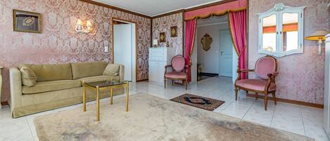 A living room with a beige sofa, a glass coffee table, two chairs, a patterned rug, and a decorative mirror.
