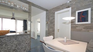 A modern kitchen with granite countertops, a white dining table, and a hanging light fixture. - Haus Metropol 175 OB (Westerland)