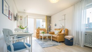 A modern living room with a sofa, armchair, and a dining table with chairs. - Haus Birgit 6-15 Steinmannstraße 15. In Zentraler und Strandnaher Lage in Westerland, Liegt Diese Gemütliche, Liebevoll Eingerichtete Ferienwohnung. Nur 100m von der Promenade/strand Sowie den Kureinrichtungen und Schwimmbad en (Westerland)