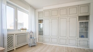 A spacious room with large windows, a built-in cabinet with glass doors, and a small table with a lamp. - Haus Birgit 6-15 Steinmannstraße 15. In Zentraler und Strandnaher Lage in Westerland, Liegt Diese Gemütliche, Liebevoll Eingerichtete Ferienwohnung. Nur 100m von der Promenade/strand Sowie den Kureinrichtungen und Schwimmbad en (Westerland)