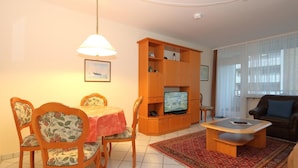 Una sala de estar con una mesa de comedor, sillas, un televisor, un sofá y un tapete estampado.