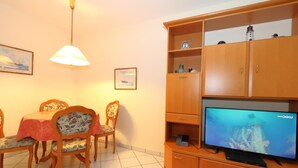 Una sala de estar con una mesa de comedor, sillas, un televisor y armarios de madera.