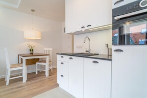 Een kleine keuken met witte kastjes, een zwart aanrecht, een roestvrijstalen spoelbak en een Bosch oven.
