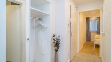 A hallway with a white wardrobe, a hanging garment, and a vase with flowers.
