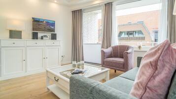 A modern living room with a grey sofa, a white cabinet, a television, and a window with curtains.