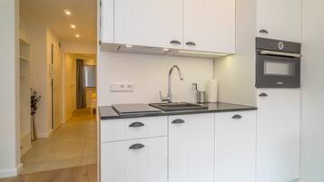 A modern kitchen with white cabinetry, a black countertop, a Bosch oven, and a stainless steel faucet.