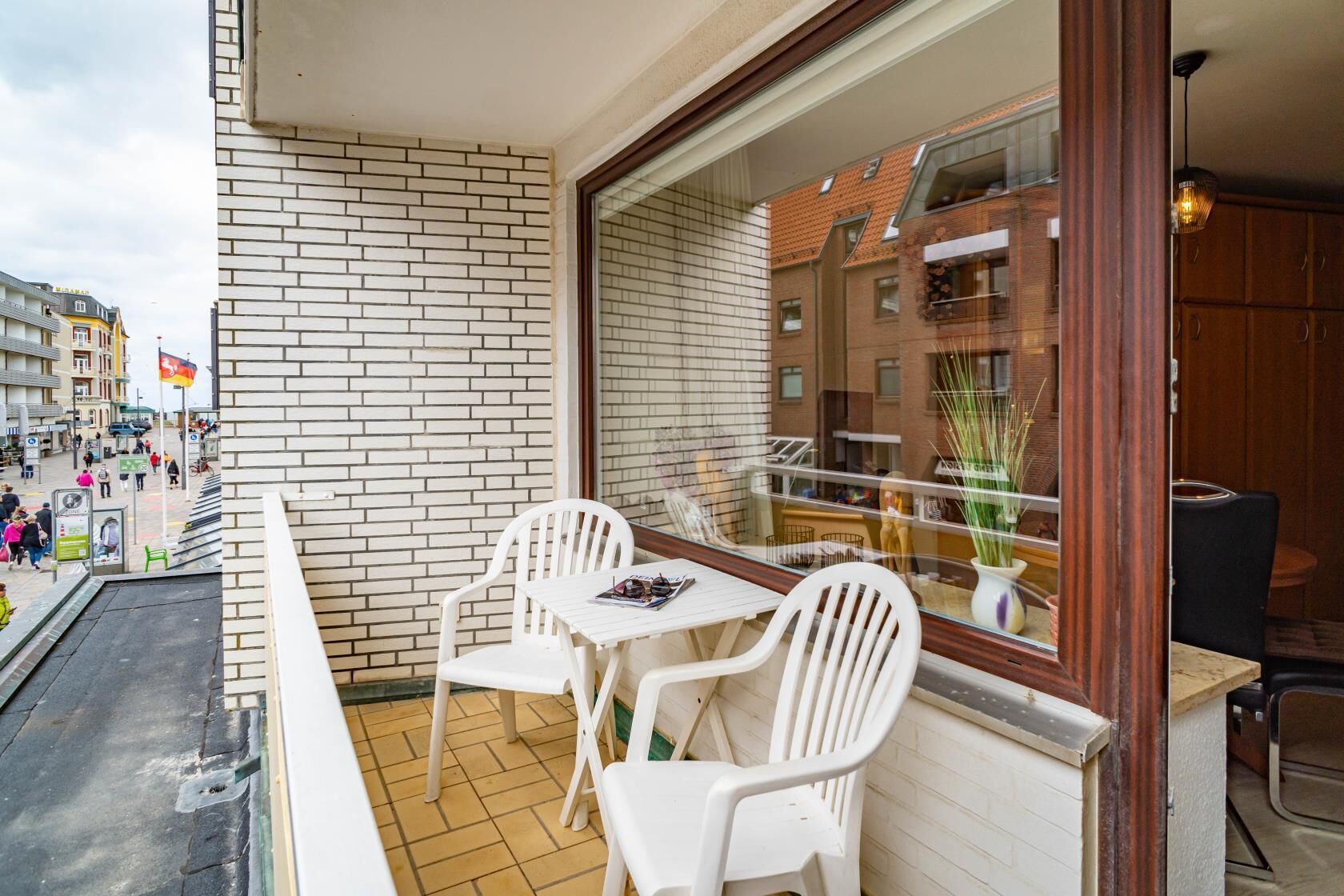 Un balcon avec des chaises et une table en plastique blanc, un mur de briques et une vue sur une rue de la ville.