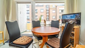 Ein modernes Wohnzimmer mit einem runden Holztisch, schwarzen Ledersesseln und einem Flachbildfernseher.