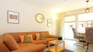 Ein Wohnzimmer mit einer Couch, einem Couchtisch, einem Sessel, einer Stehlampe und einem großen Fenster mit Vorhängen.