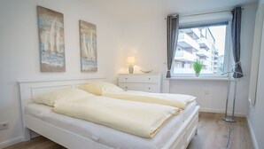 Una camera da letto con un letto, due quadri, un comodino con una lampada, una finestra con tende e una pianta in vaso.