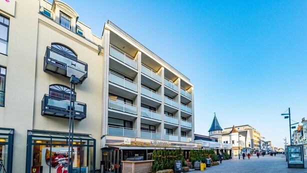 Un edificio a più piani con un caffè e un ristorante al piano terra, posti a sedere all'aperto e un cielo blu limpido.