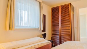 A hotel room with two single beds, a window with curtains, a radiator, and a wooden wardrobe. - Windhuk 1-11 am Strand (Westerland)