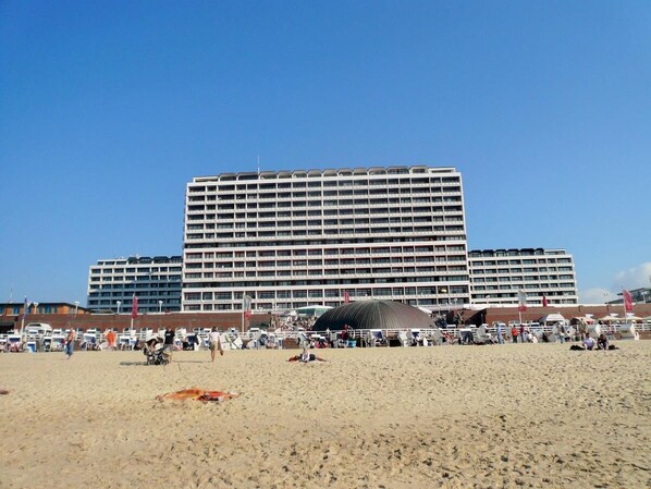 A large hotel with multiple floors and balconies, situated on a beach with a sandy foreground and a clear blue sky. - Haus Metropol 277 OB (Westerland)