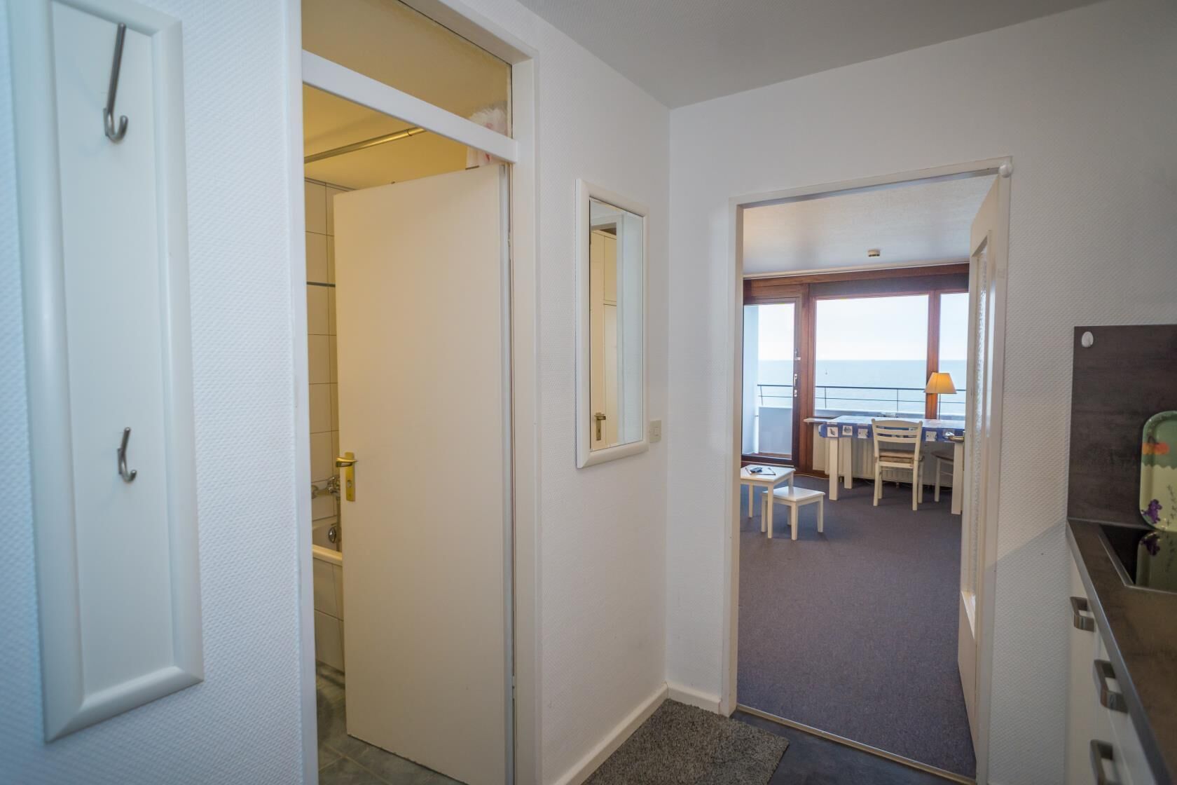 A hallway leading to a balcony with a table and chairs, a view of the sea, and a bathroom with a shower and toilet.