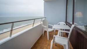 Un balcon avec vue sur la plage et l’océan. On y trouve deux chaises en plastique blanches et une petite table.