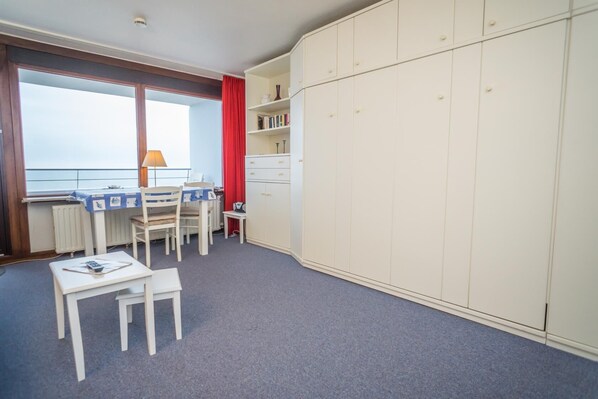 A room with a desk, chairs, a radiator, a window with curtains, and a wardrobe.