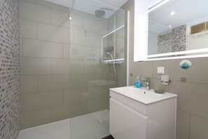 Een moderne badkamer met een douchecabine van glas, een witte wastafel en een spiegel.