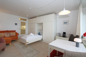 Een slaapkamer met een bed, kledingkast, bureau en een klein tafeltje met een lamp.
